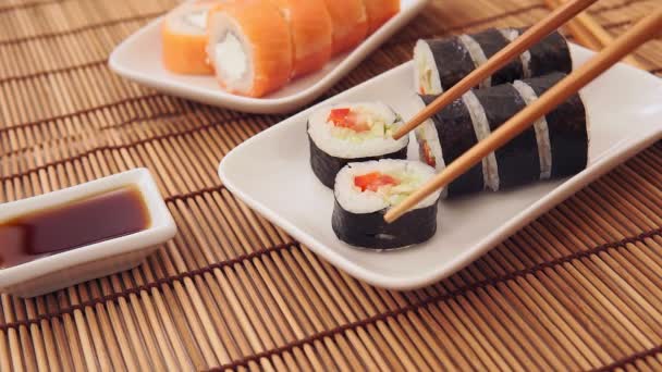 Close up of chopsticks holds sushi maki roll over a plate or platter set. — Vídeo de Stock