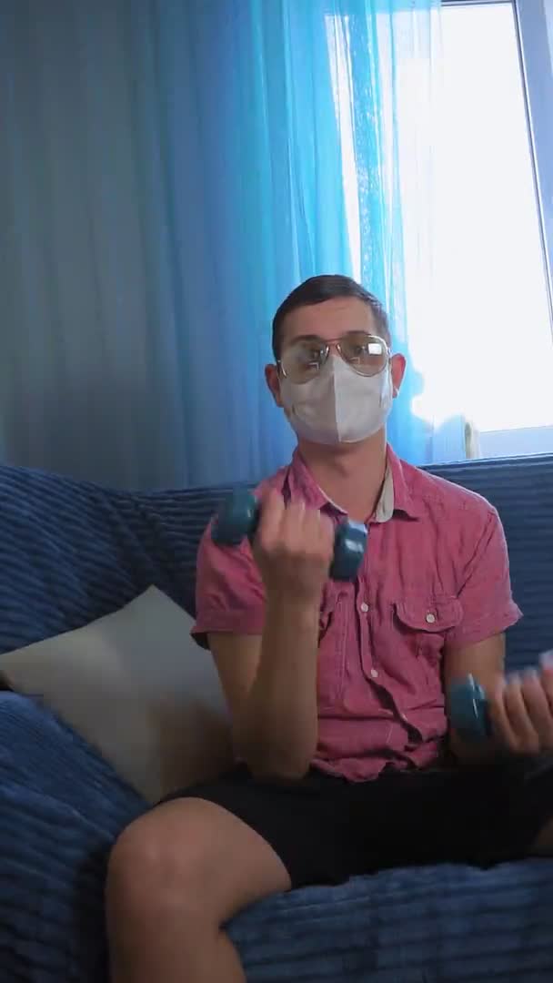 Een jongeman met halters in een masker van een coronavirus. humor verticale video. — Stockvideo