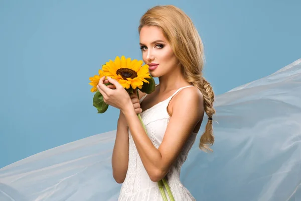 Porträt einer attraktiven Sommerfrau mit Sonnenblume in der Hand auf blauem Hintergrund — Stockfoto