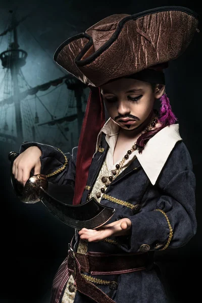 生气的小男孩穿着海盗服装。他站在船的背景 — 图库照片