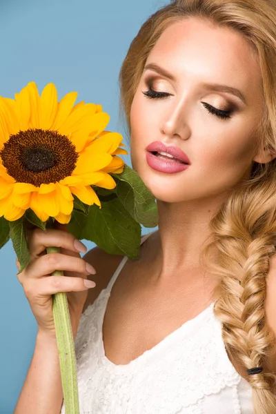 Porträt einer attraktiven Sommerfrau mit Sonnenblume in der Hand auf blauem Hintergrund — Stockfoto