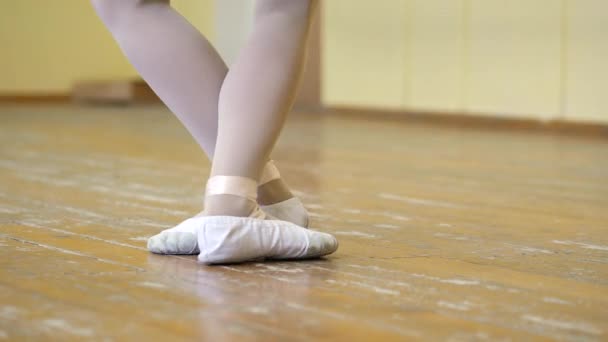 Primer plano de las piernas de una niña en zapatos de ballet blanco en un piso de madera viejo durante el entrenamiento de ballet. Elemento del ejercicio de danza clásica . — Vídeos de Stock