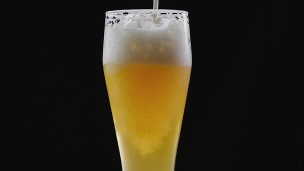 Bier is gieten in glas op zwarte achtergrond. Zeepbellen en schuim in bierglas. Schuim glijdend van het glas bier. Het vullen van bier in het glas. bier bubbels. Bier ingeschonken glazen op zwarte achtergrond. — Stockvideo