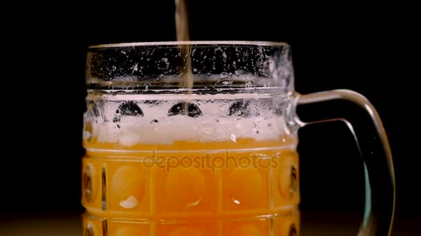 Bier wird auf schwarzem Hintergrund ins Glas gegossen. Schaumstoff gleitet schnell durch das Glas. Extrem großer Bierschaum und Blasen. voller Becher bernsteinfarbenes Bier auf schwarzem Hintergrund. Zeitlupe. — Stockvideo