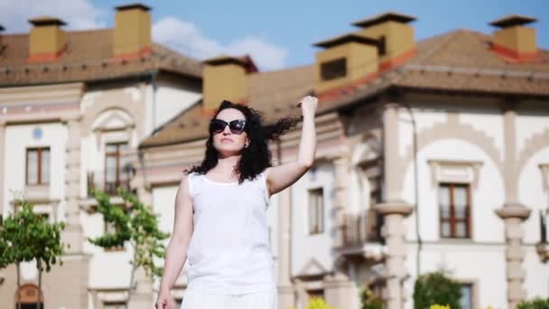 A happy woman adjusts her hair in the wind, slow motion. Young beautiful brunette in white dress smiles, relaxes and enjoys life. A woman with glasse — Stock Video