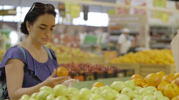 Atractiva joven morena elige frutas - naranja fresca - en el supermercado. Compras y concepto de personas. Imágenes de vídeo de archivo. 4k . — Vídeos de Stock