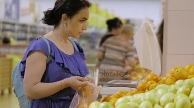 Çekici genç kadın brunet meyve - taze turuncu - süpermarkette seçer. Alışveriş ve insanlar kavramı. Stok video görüntüleri. 4k.