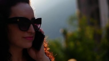 Gözlüklü beyaz elbiseli uzun ateşli kıvırcık saçlı güzel bir esmer şehirde yürüyüş ve gün batımında Evet