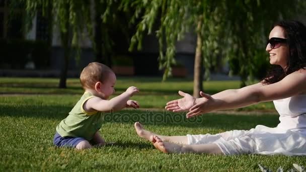 Ungen drar hans mors händer. Barnet tar de första stegen. Mamma leker med barnet. — Stockvideo