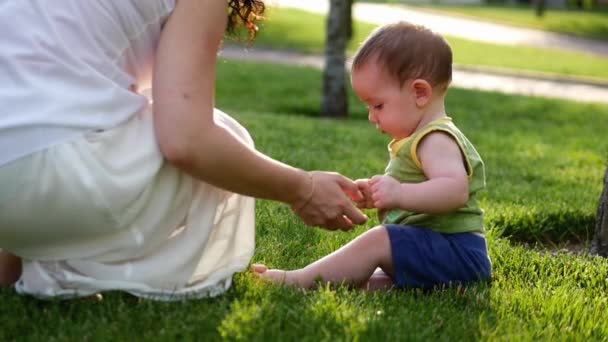 Mutter behält die Unterarme des Kindes, lehrt, die ersten Schritte zu tun. das Baby macht die ersten Schritte. Mutter spielt mit dem Kind. — Stockvideo