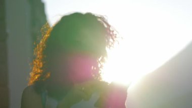 Gözlüklü beyaz elbiseli uzun ateşli kıvırcık saçlı esmer güzel şehirde yürüyüş ve sms telefonda günbatımında tipik.