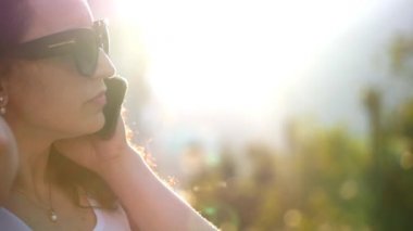 Gözlüklü beyaz elbiseli uzun ateşli kıvırcık saçlı güzel bir esmer şehirde yürüyüş ve gün batımında Evet