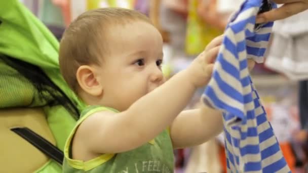 Mamá compra ropa de bebé. El bebé está contento con la compra . — Vídeos de Stock