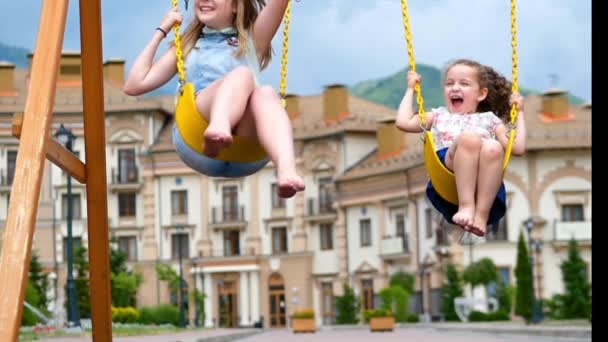 Les petites filles font une balançoire. Deux petites sœurs profitent de la vie sur les balançoires . — Video