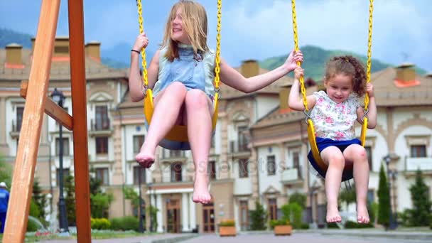 Las niñas montan en un columpio. Dos hermanitas disfrutan de la vida en los columpios . — Vídeos de Stock