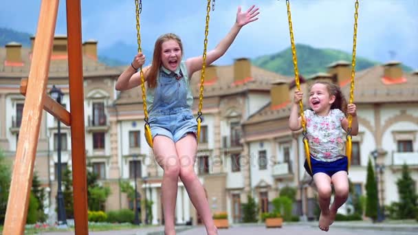 Les petites filles font une balançoire. Deux petites sœurs profitent de la vie sur les balançoires . — Video