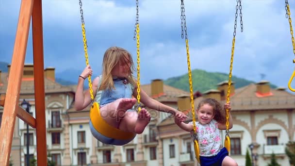 Les petites filles font une balançoire. Deux petites sœurs profitent de la vie sur les balançoires . — Video