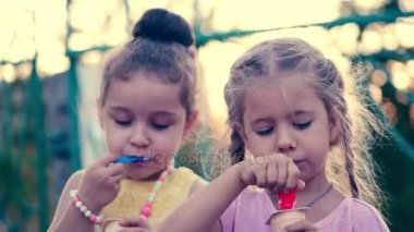İki küçük kız arkadaşlarıyla kıvırcık sarı saçlı mavi gözlü dondurma yeme ve gülüyor.