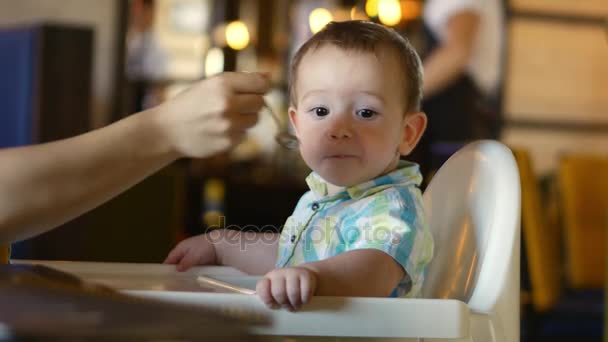 Crianças e comida, a mãe dá comida de bebê de uma colher de bebê em um restaurante, a criança se entrega e se recusa a comer. 4k . — Vídeo de Stock