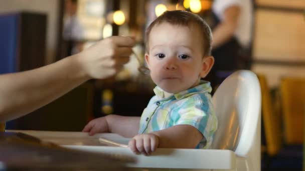 Crianças e comida, a mãe dá comida de bebê de uma colher de bebê em um restaurante, a criança se entrega e se recusa a comer. 4k . — Vídeo de Stock