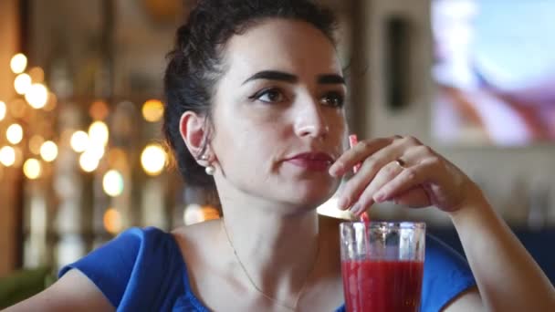 Una giovane e attraente bruna, vestita di blu con pizzo, si siede in un caffè e beve cocktail. 4K . — Video Stock
