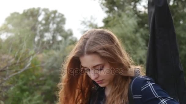 Een jong mooi meisje loopt in het bos, met een gitaar op haar schouder. Zonsondergang zonsondergang — Stockvideo