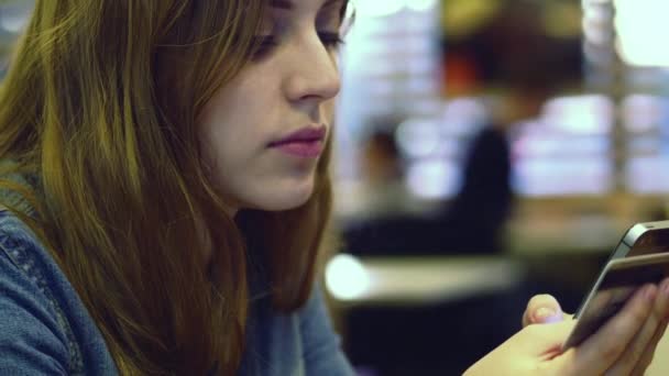 Teen girl pays with a credit card on smartphone in cafe. 4K. — Stock Video