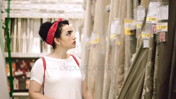 An attractive young woman with pronounced features of Caucasian appearance chooses a new interior for the house, looks at carpets and curtains, tulle and curtains. — Stock Video