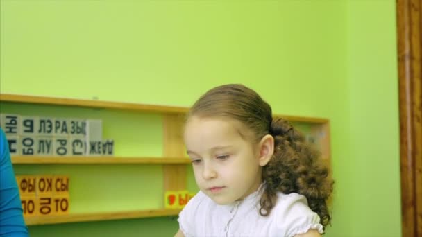 Una niña que estudia las lecciones, una niña bonita hace su trabajo escolar junto con la maestra, desarrolla el habla y la motilidad utilizando cubos de colores brillantes con letras y animales. 4K . — Vídeos de Stock