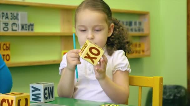 Schöne kleine Schulmädchen mit einer schönen Frisur und einem schönen Lächeln in einer weißen Bluse sitzt an ihrem Schreibtisch mit einem Lehrer und unterrichtet Fremdsprachen, führt die Aufgabe eines Lehrers richtig sprechen und Wörter aussprechen, um die Aussprache zu kennen und — Stockvideo