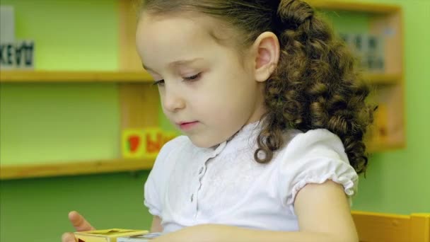 Uma menina estudando as lições, uma linda menina faz seus trabalhos escolares junto com o professor, desenvolve fala e motilidade usando cubos coloridos brilhantes com letras e animais. 4K . — Vídeo de Stock