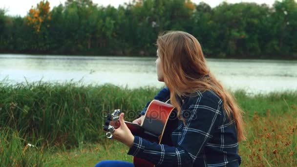 女手弹吉他。一个快乐的无忧无虑的年轻女孩弹吉他，虽然她是在树林里孤单，当太阳开始设置. — 图库视频影像