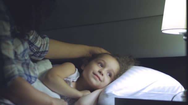 Mooie moeder geeft een anterior kus haar kind voordat het naar bed gaan, zachtjes knuffels van het kind en haar zeer zoet te bedekken met een deken en schakelt de lamp. 4k — Stockvideo