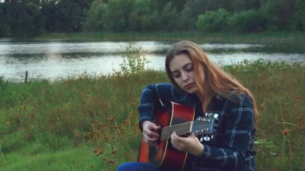Hipster ung vacker flicka, omfamnas av en kreativ start i en glänta i skogen vid middagstid, inspirerad av ett skogslandskap med utsikt över floden och häpnadsväckande natur, plockar upp en ny melodi för en ny — Stockvideo