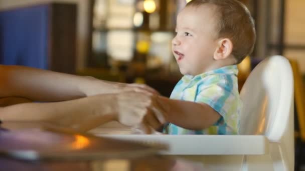 Moeder veegt haar mond en handen op de schattige baby. Een charmante kind lacht en klapt. 4k. — Stockvideo