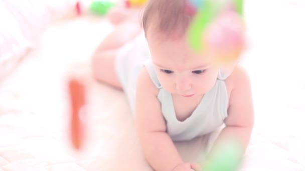 귀여운 작은 아이 카메라에서 외모와 흰색 침대와 행복. 아이는 장난감 개발에 매달려 고려 측면에서 보이는. — 비디오