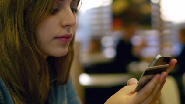 Teen girl pays with a credit card on smartphone in cafe. 4K. — Stock Video