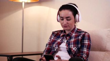 Boynundaki bir smartphone, cep telefonunda mesaj üzerinde bir uygulama kullanarak kulaklıklarla oturan güzel genç beyaz kadın.