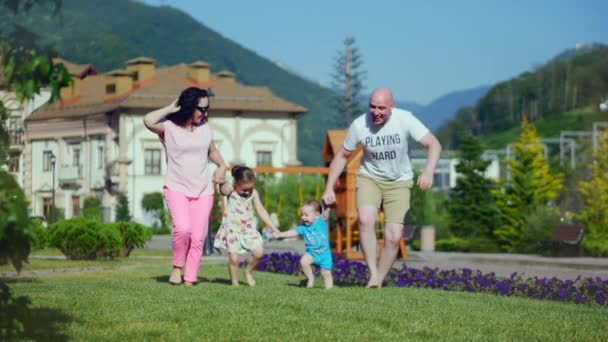 Unbekümmerte junge kaukasische Familie läuft fröhlich über das grüne Gras, Händchen haltend, glückliche Gesichter der Familie. — Stockvideo