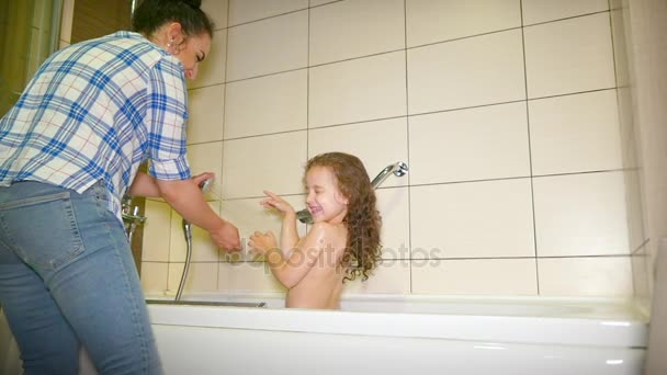 A mãe lava a cabeça de uma criança pequena. A mãe a lavar o bebé com champô num banho de espuma. O miúdo fica feliz quando a mãe lhe põe água na cabeça. . — Vídeo de Stock