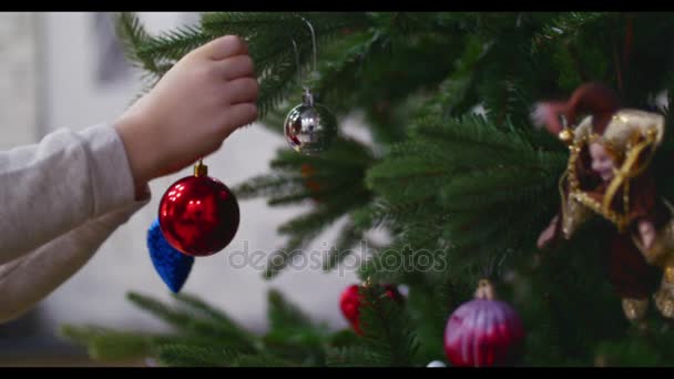 Повесить рождественское украшение на елку с рождественскими огнями. Украшение рождественской елки мячом. 4K — стоковое видео