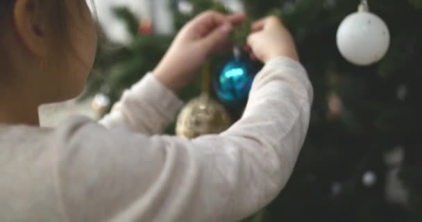 Weihnachtsschmuck am Baum mit Weihnachtsbeleuchtung aufhängen. Weihnachtsbaum mit Kugel dekorieren. 4k — Stockvideo