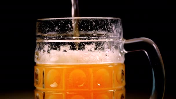 Bier wordt gegoten in het glas op een zwarte achtergrond. Schuim snel glijdt door het glas. Volledige mok amber bier op een zwarte achtergrond. Slow Motion. — Stockvideo