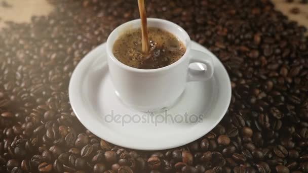 Koffiekopje en koffiebonen. Een witte kop koffie op de tabel met geroosterde bonen verdampen. Slow Motion koffie pour. — Stockvideo