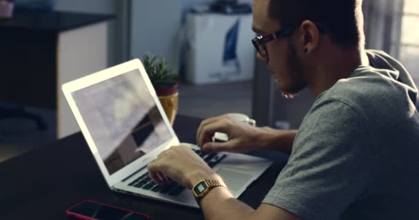 Молодой бизнесмен в очках с часами на руках, сидит за столом, работает за компьютером. 4K — стоковое видео