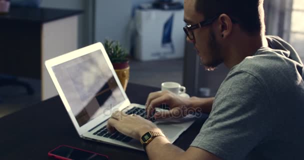 Jeune homme d'affaires portant des lunettes avec une horloge sur les mains, assis à une table, faisant du travail sur l'ordinateur. 4K — Video