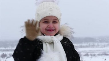 Onun sokakta, kar yağışı kışın 5 yaşında küçük bir kız elini sallayarak ve temiz havada gülümseyerek kameraya, görünüyor. Ağır çekim.