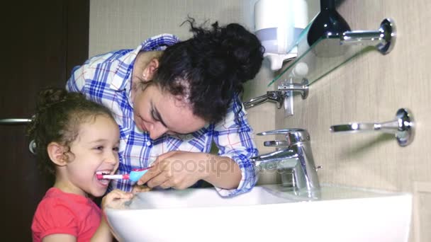 Mãe suavemente escova os dentes de sua amada filha Uma menina com sua mãe limpa suavemente os dentes depois de comer. 4k . — Vídeo de Stock