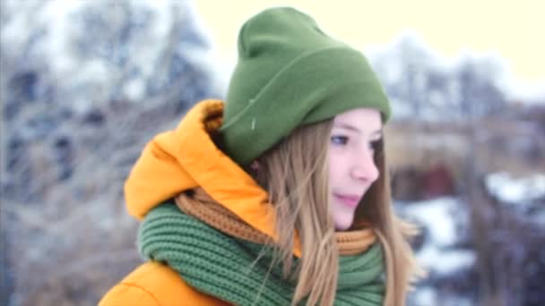 Portrait of a young beautiful teenage girl with blond hair, in the beautiful nature of a winter forest, girl with a green and brown scarf in a green hipster hat, walking outdoors, looking at the — Stock Video