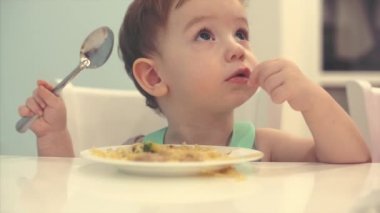 Küçük çocuk bir önlük bir masada oturan ve kendi spagetti yemek bebek yiyor isteyerek.
